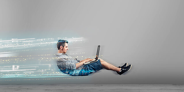 Ein Mann arbeitet mit einem Laptop, während leuchtende digitale Datenspuren Geschwindigkeit und eine schnelle Internetverbindung symbolisieren.